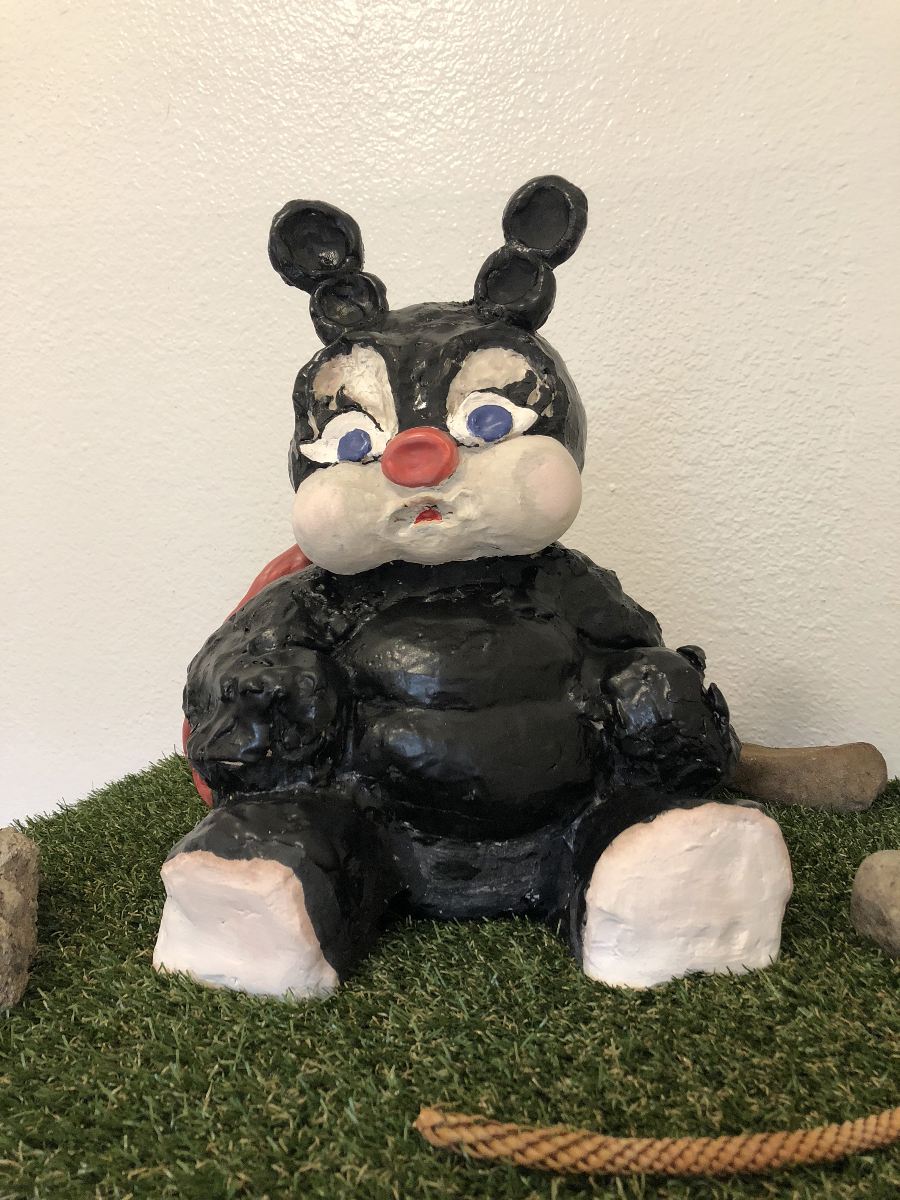 Detail of a ceramic sculpture of a black ladybugy on a small table covered in astroturf